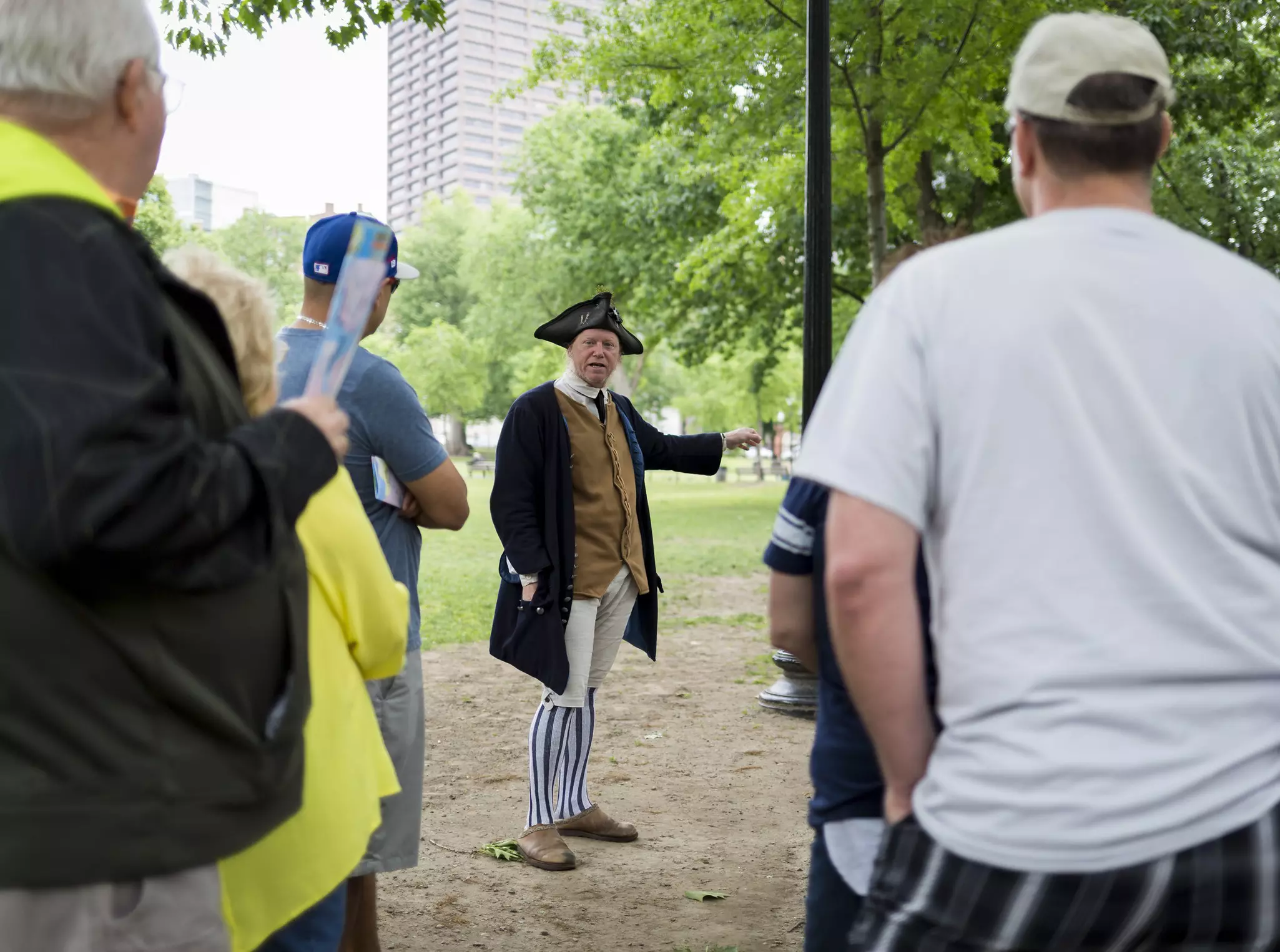 A person in colonial garb talks to a group of tourists in a public park.