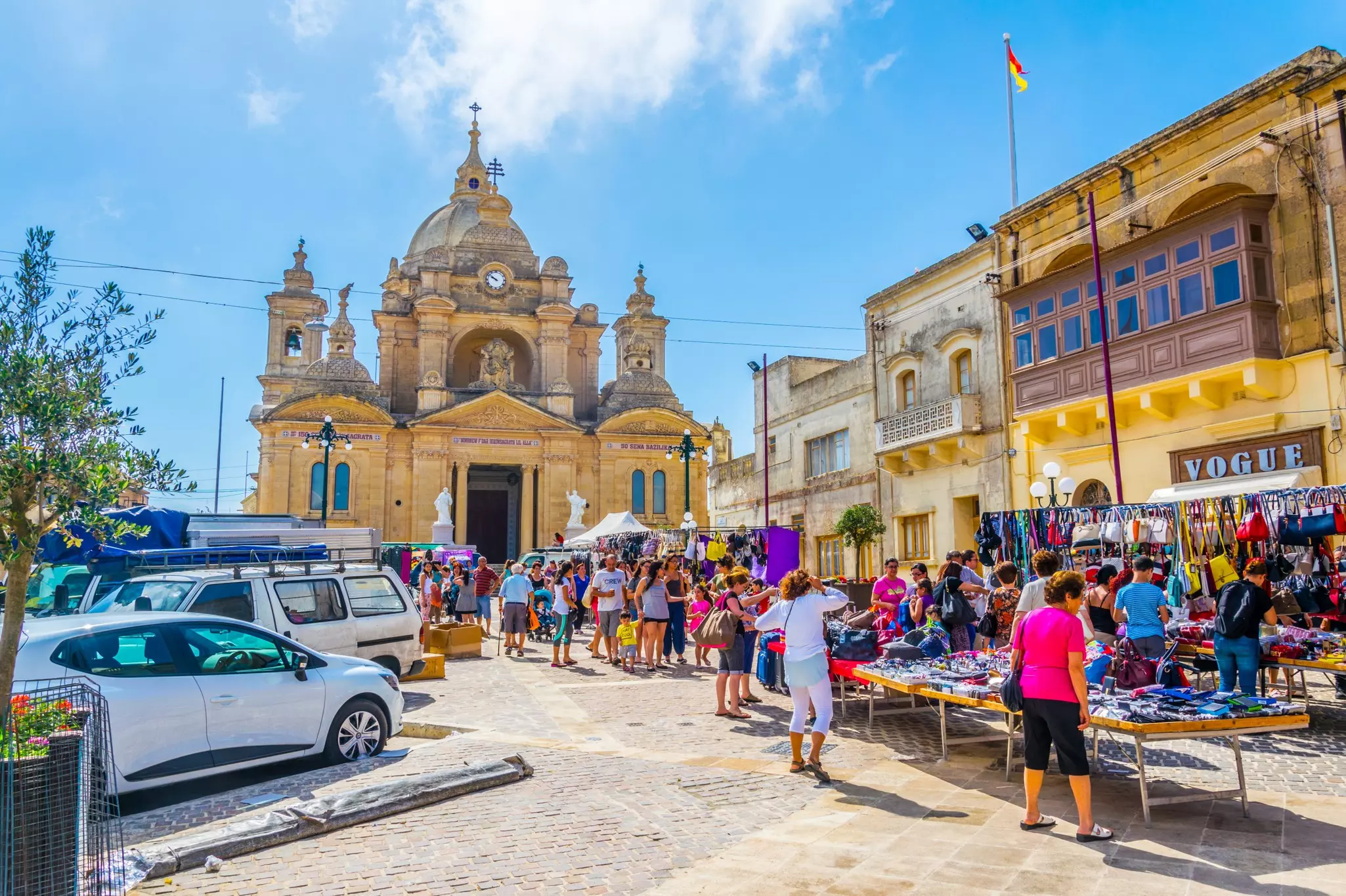 Cars parked in the main square of a small town where a busy market is ongoing.