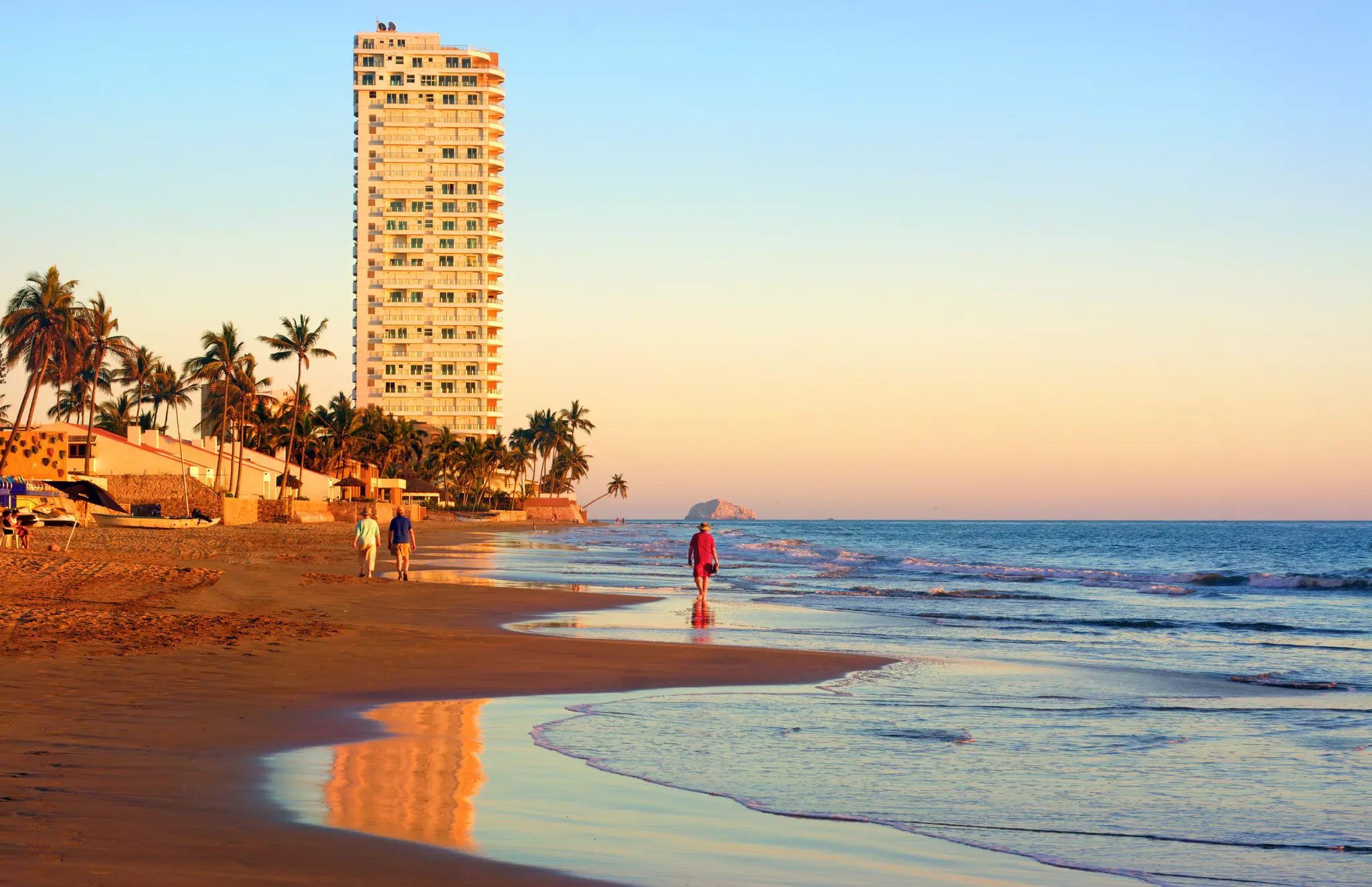 Three people walk along the seashore as the sun sets and bathes to coast in golden light