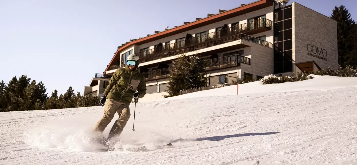 A solo male skier speeds by the front of a hotel: COMO Hotels & Resorts, the Dolomites, Italy