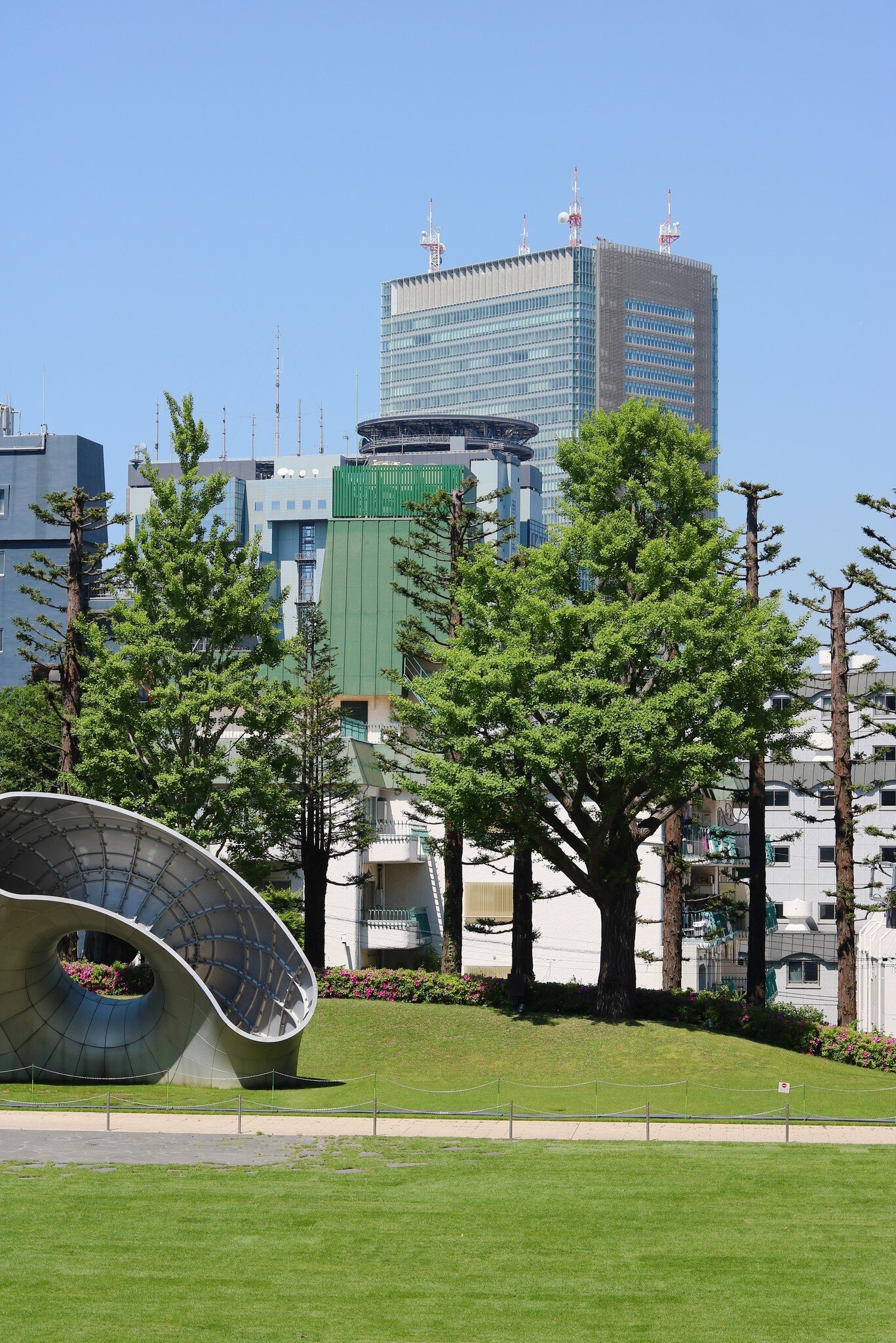 TOKYO, JAPAN - April 30, 2025: Garden of Tokyo Midtown in Roppongi with a modern sculpture and trees and skyscrapers in the background., License Type: media, Download Time: 2025-12-19T12:49:01.000Z, User: LP_YKhanna, Editorial: true, purchase_order: 65050 - Digital Destinations and Articles, job: LP, client: App Content, other: Yuvraj Khanna