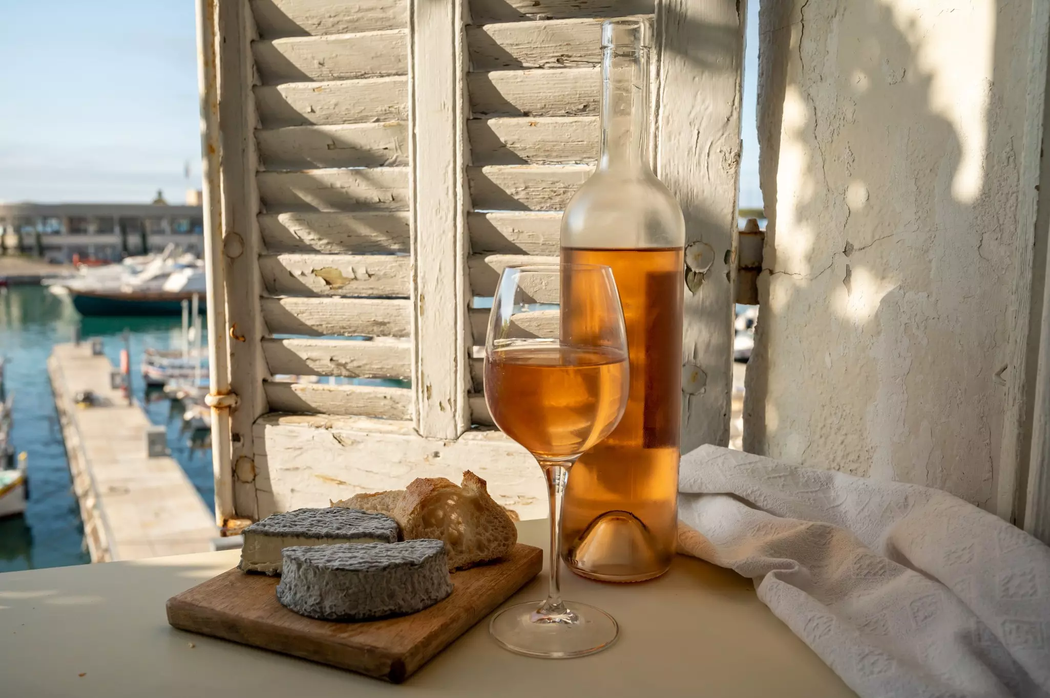 Wine in glass and bottle served with cheeses on outdoor terrace with view of a harbour