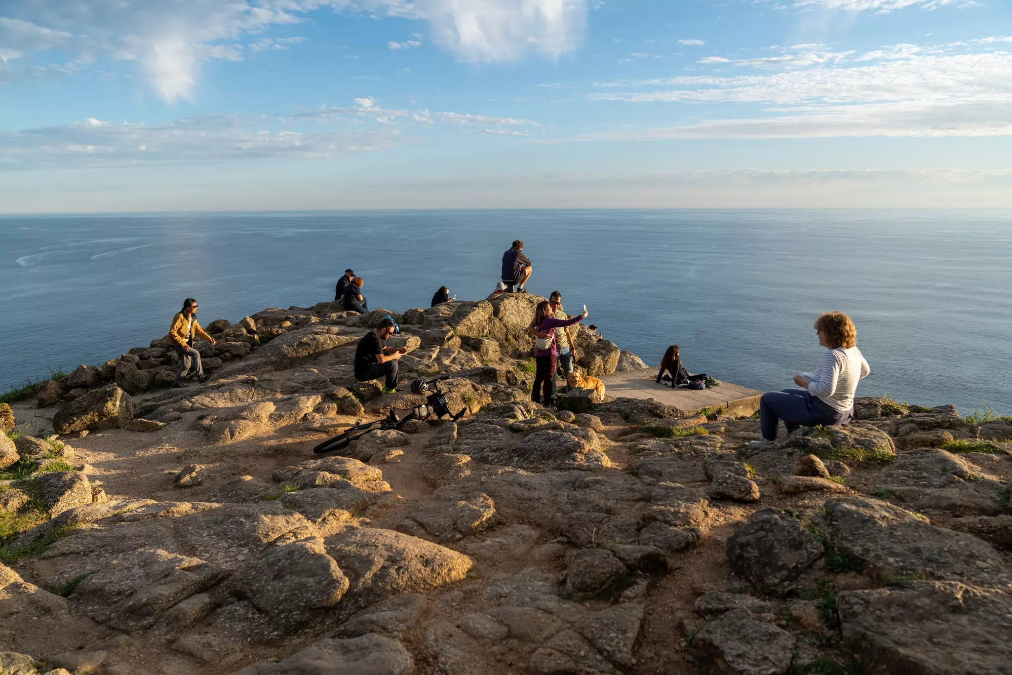 People relaxing and taking photos at Finisterre near the water.