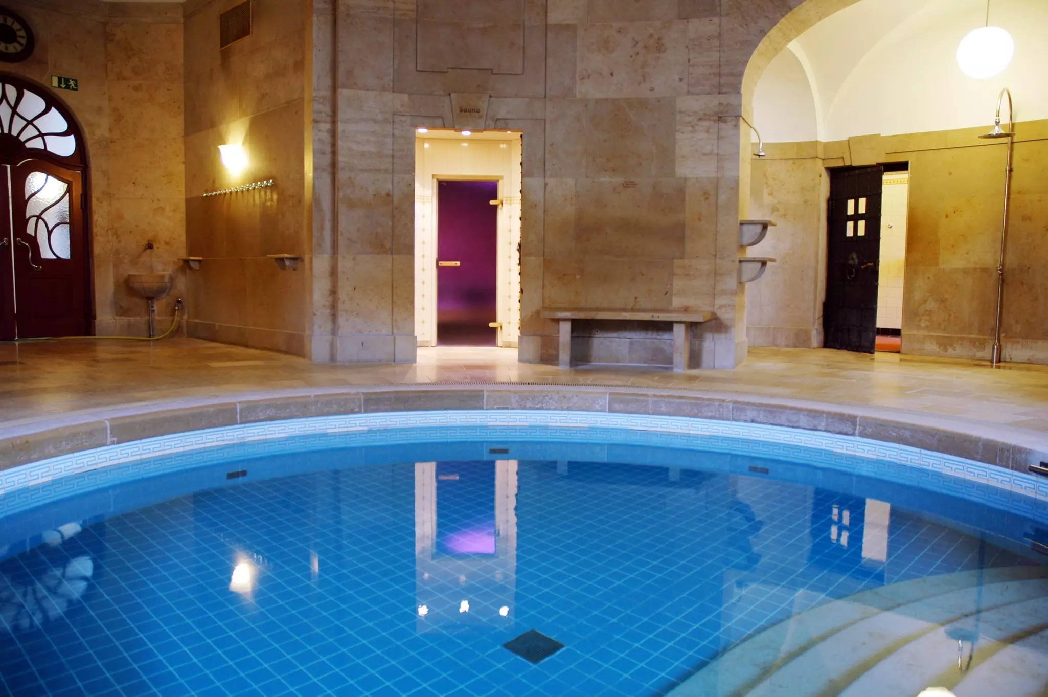 A small round pool within an indoor bathhouse. Several doors lead out of the round room.