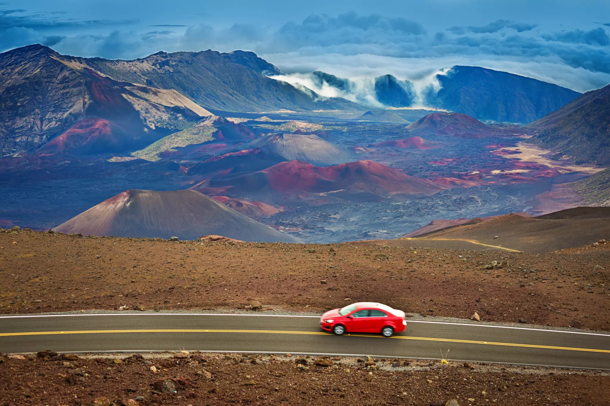 Red car drives on a curved road with Hakeakalā National Park in the background.