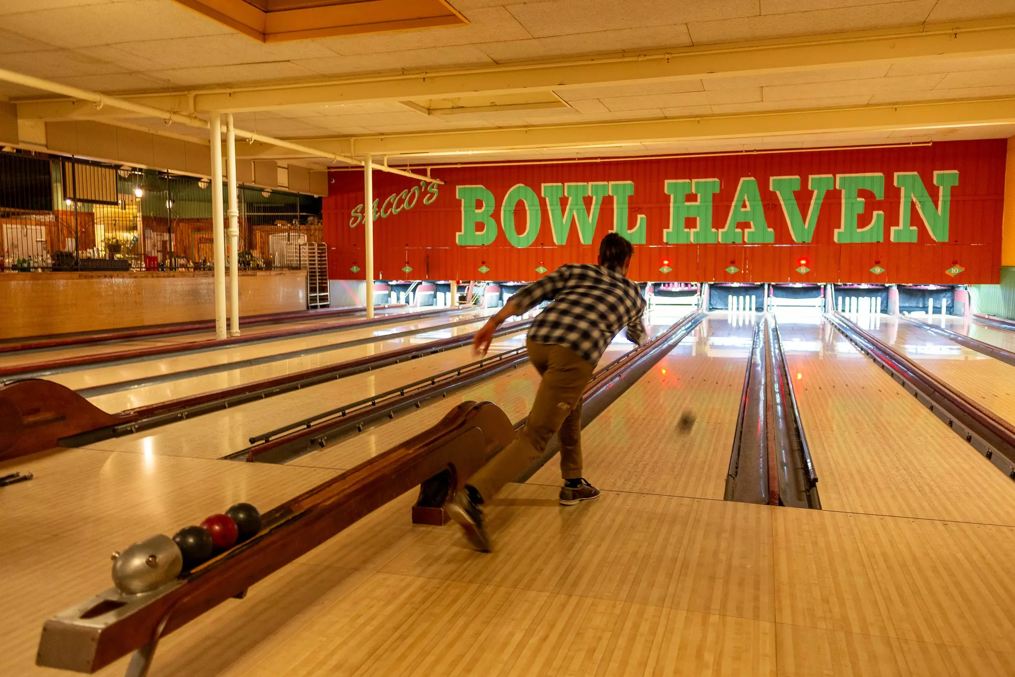 Person bowling with small ball going down a lane toward candlepins