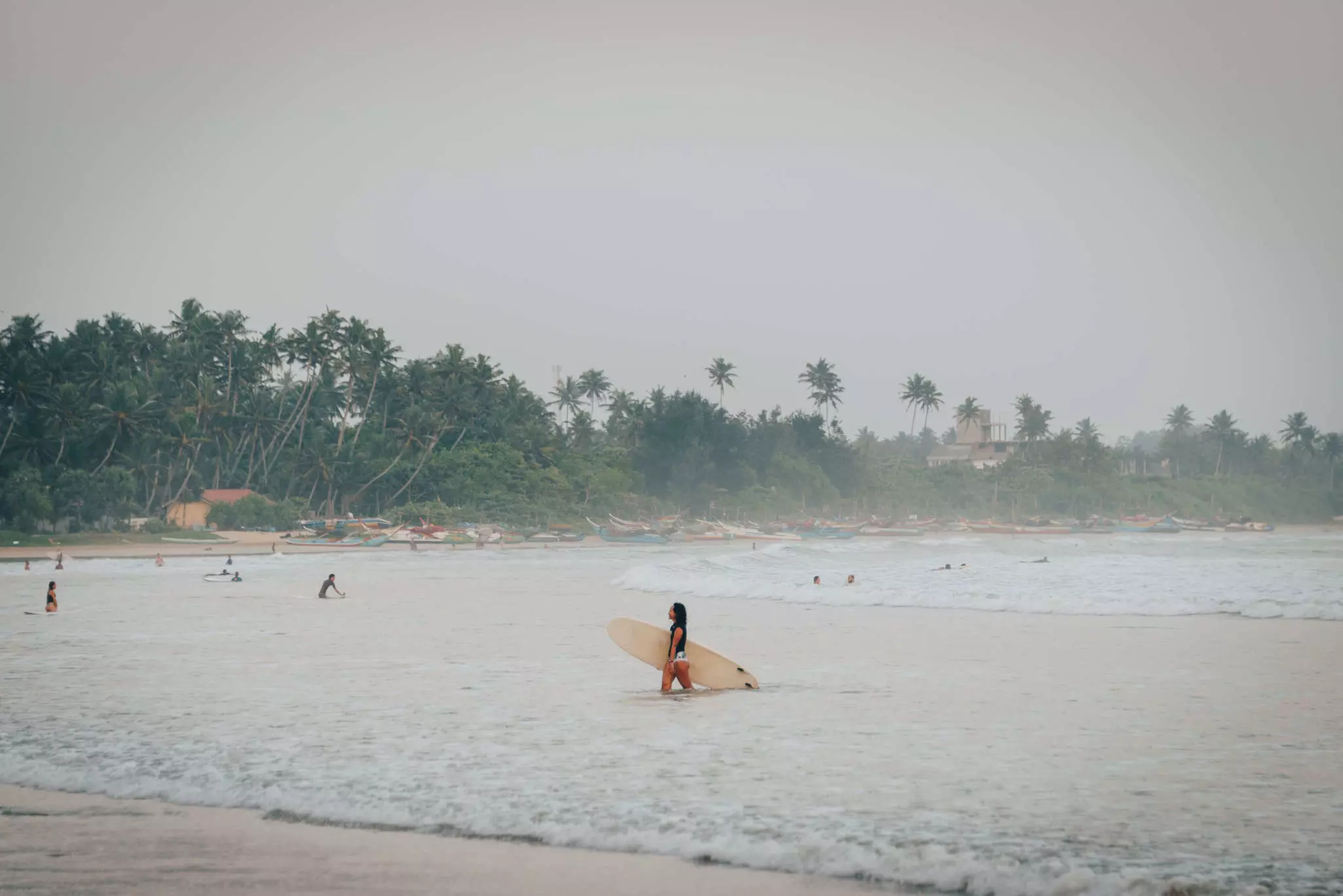 Surfers in the water at beach in Sri Lanka on a hazy, rainy day.
