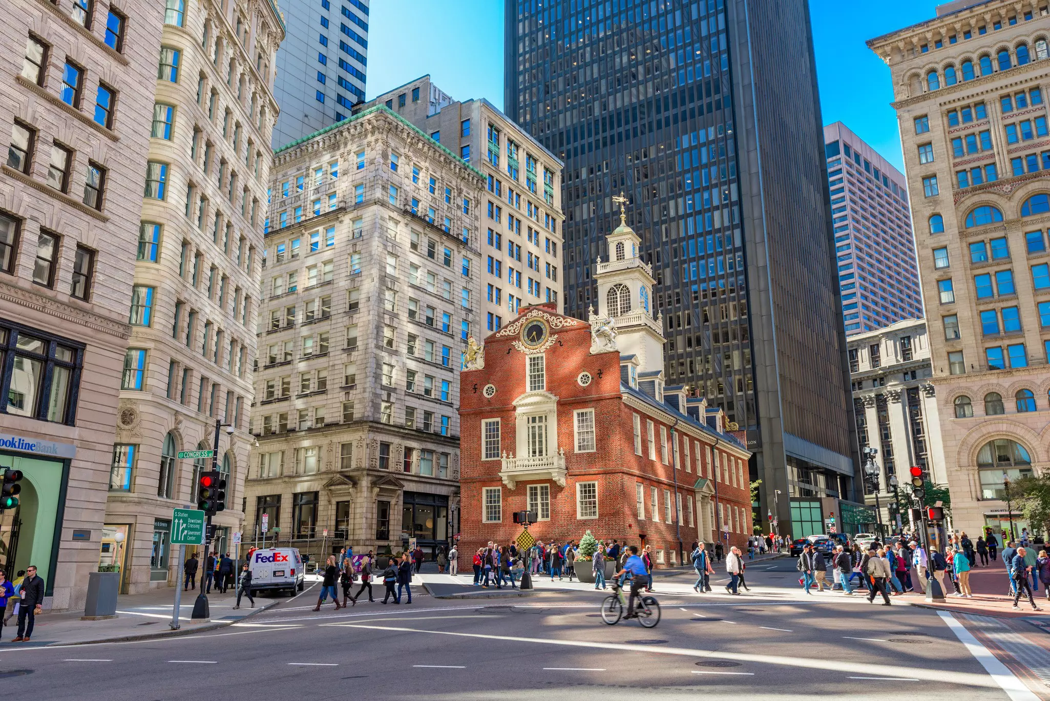 A red-brick building surrounded by high-rise towers at a busy city intersection.