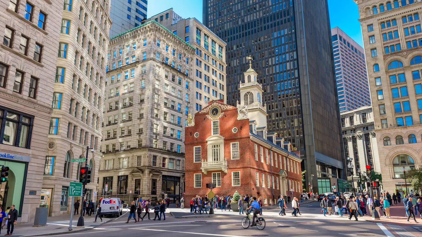 A red-brick building surrounded by high-rise towers at a busy city intersection.