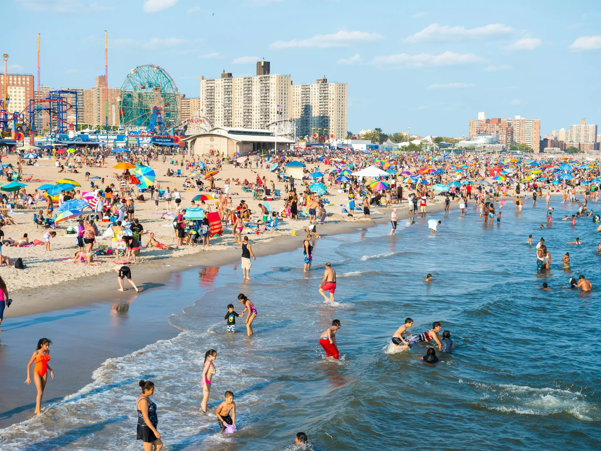 Crowds of people sunbathing and swimming at Coney Island beach. 