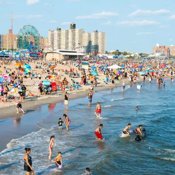 Crowds of people sunbathing and swimming at Coney Island beach. 