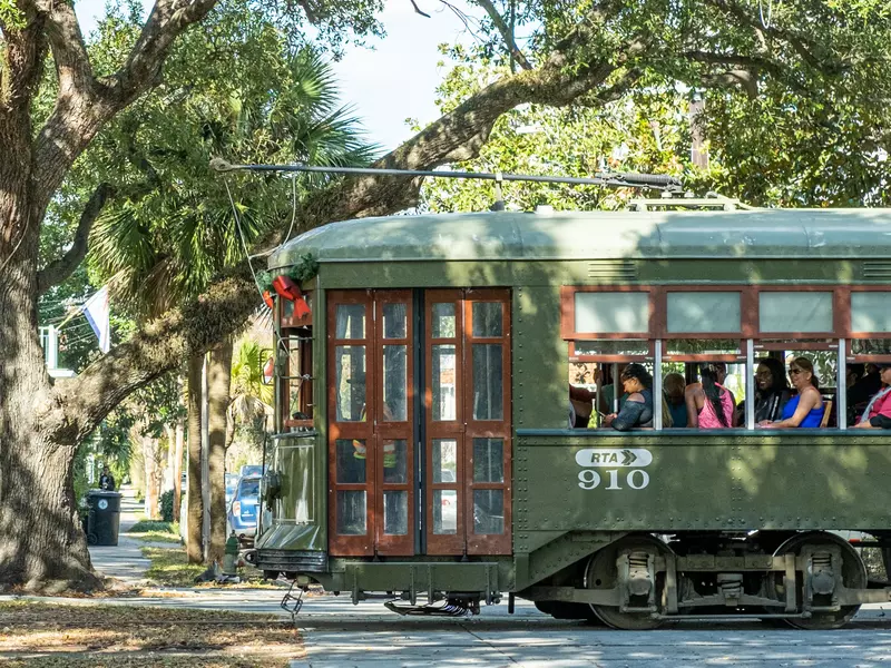 A green street car on a leafy street.