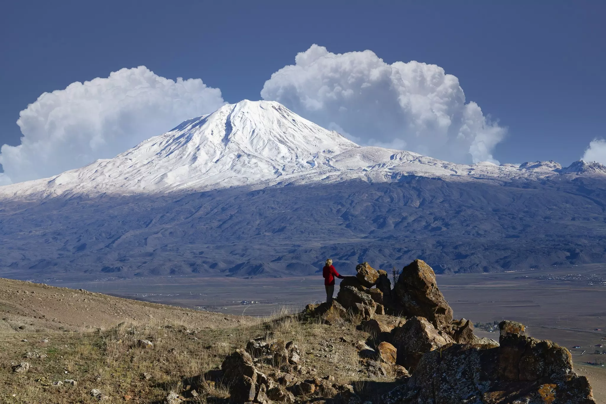 A hiker stands at a rocky cairn in front of a large snow-capped mountain in Turkey.