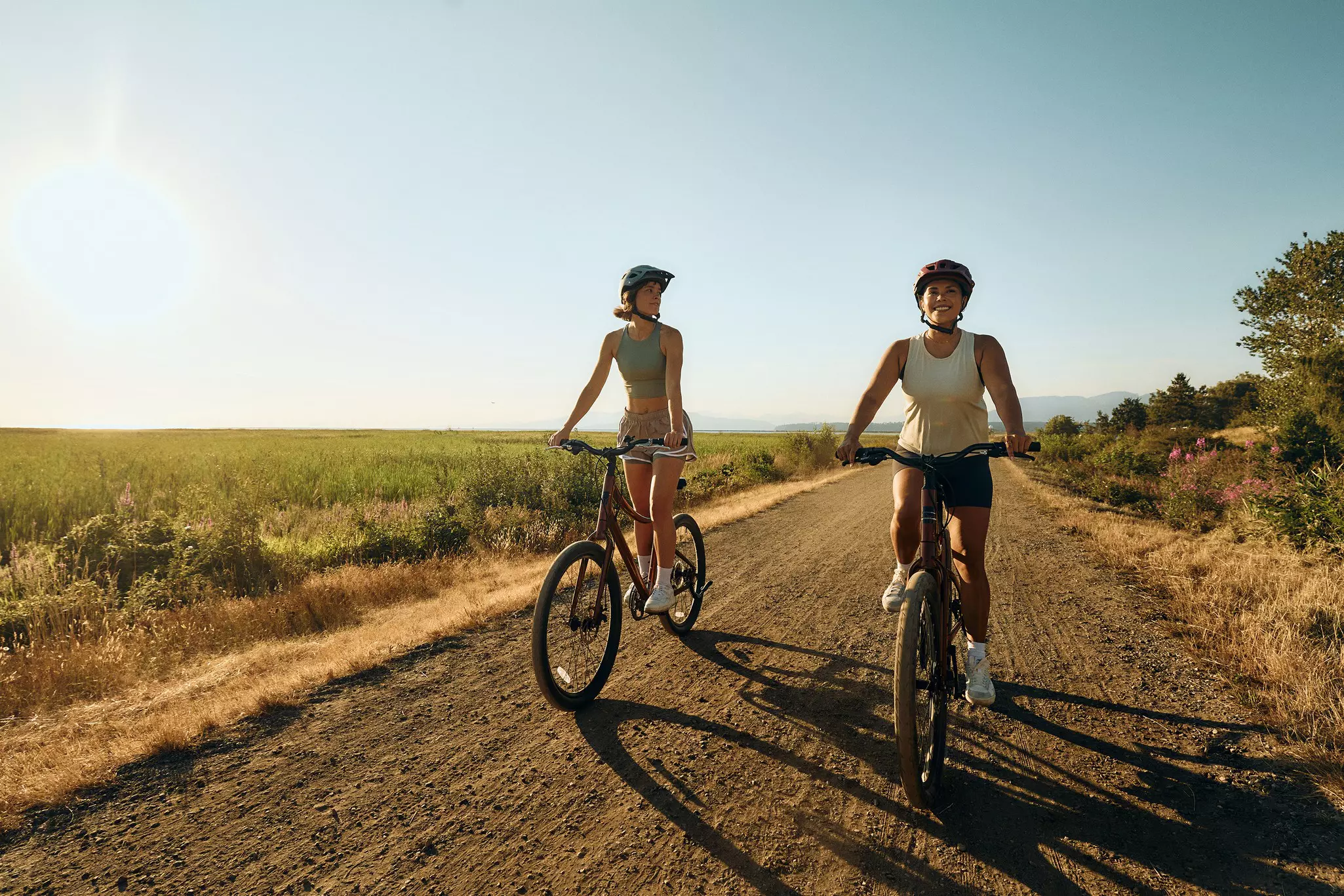 Two women on bicycles ride down a dirt path through grassland in British Columbia