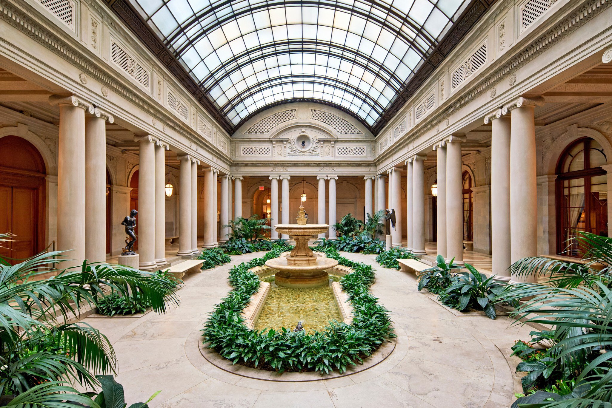 A fountain and greenery beneath the arched glass roof of the Frick's Garden Court