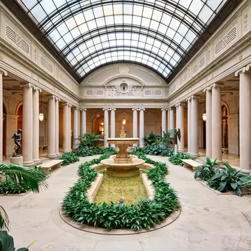 A fountain and greenery beneath the arched glass roof of the Frick's Garden Court