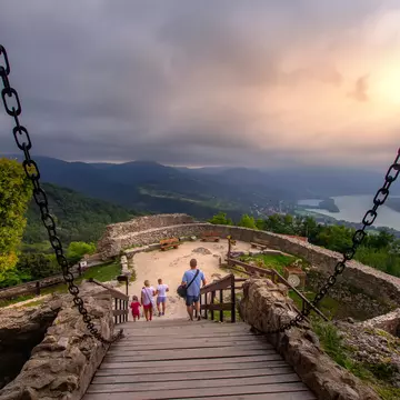 People walk down a ramp toward an overlook far above a river; a stone wall surrounds the overlook, and there are low stone walls leading to the ramp, with chains connected that rise to a point out of view.