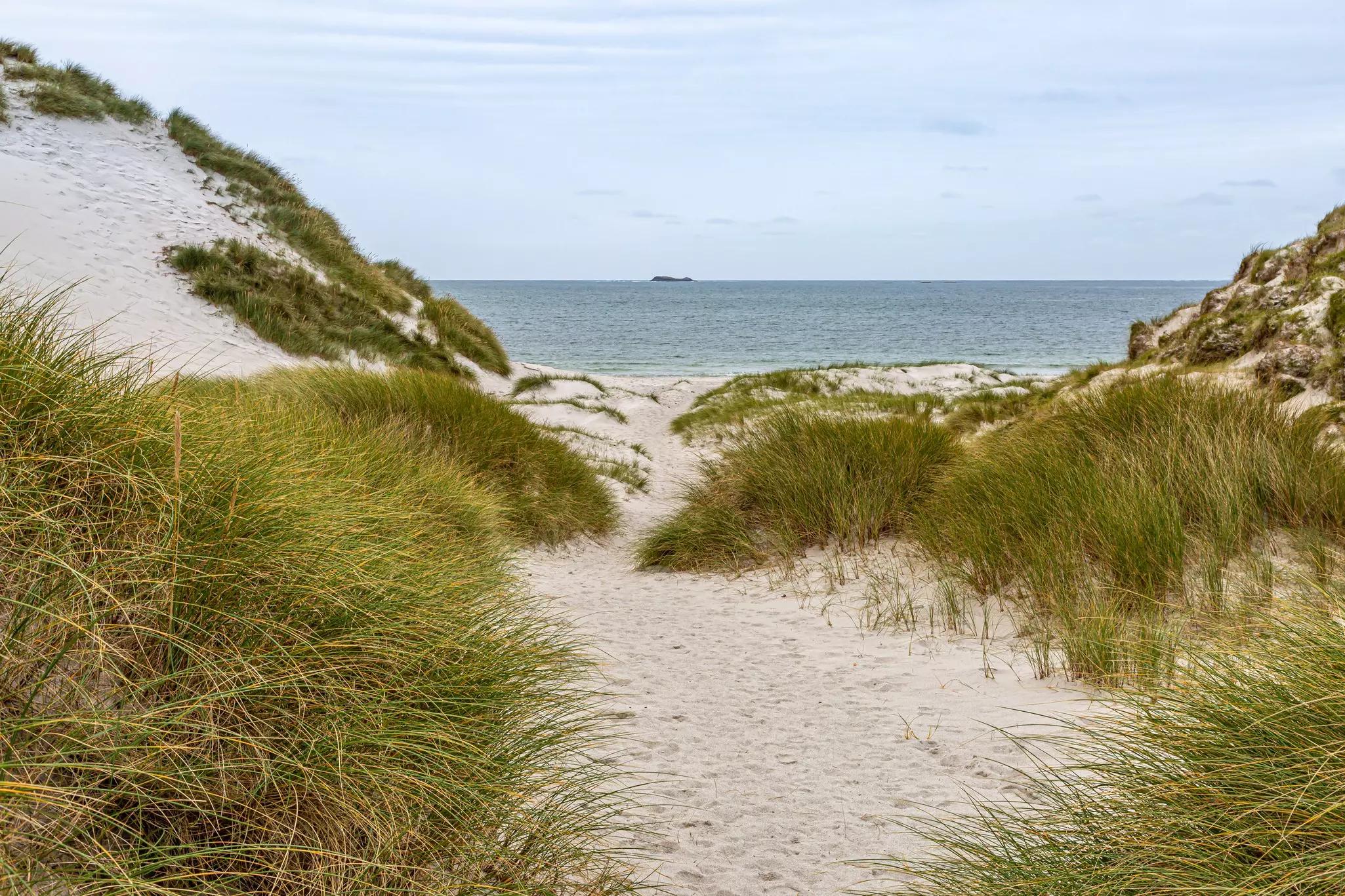 Looking through grass-covered sand dunes towards the sea on a cloudy day.