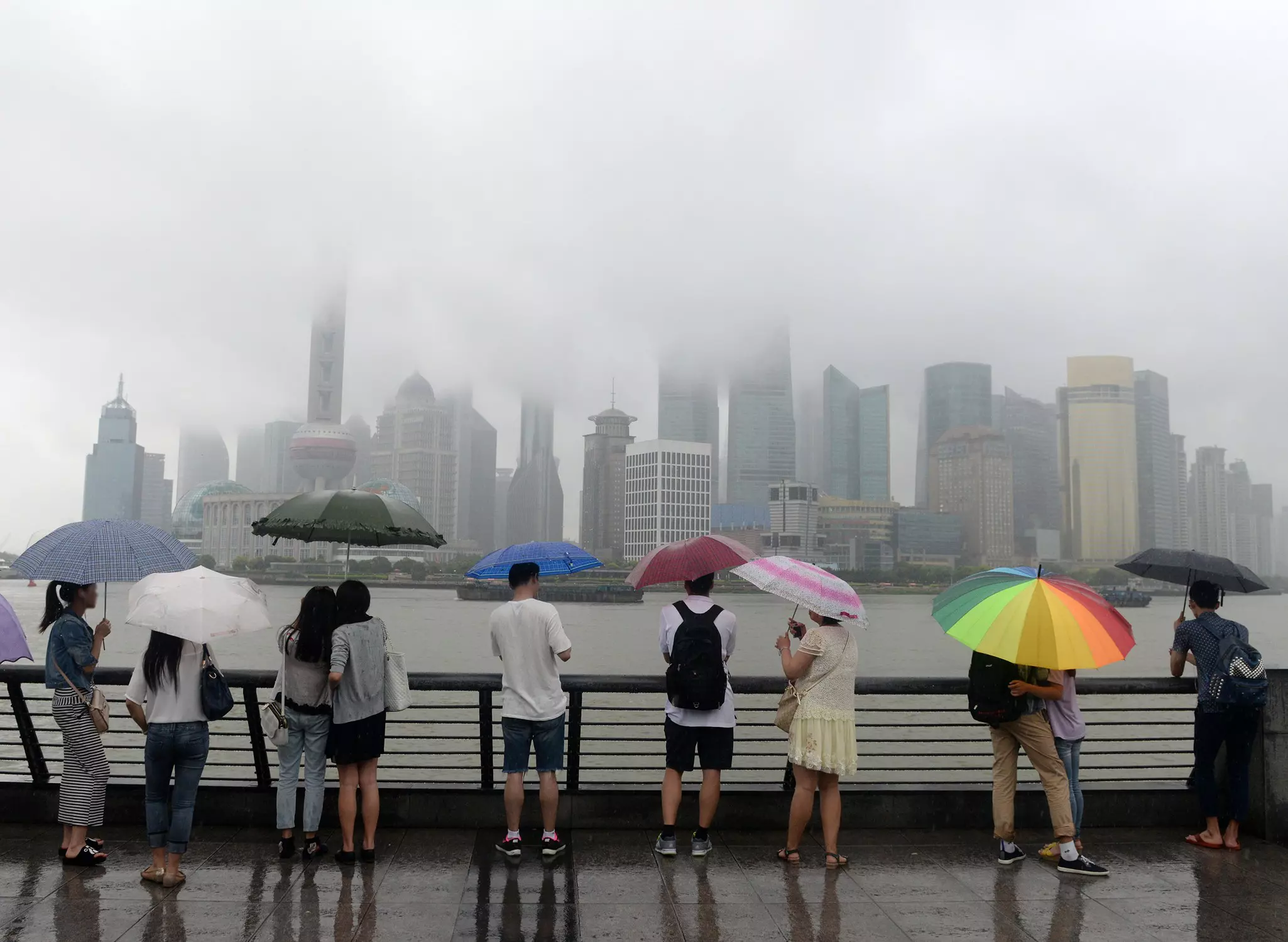 People holding umbrellas while looking at Pudong skyline across the Bund on a rainy day