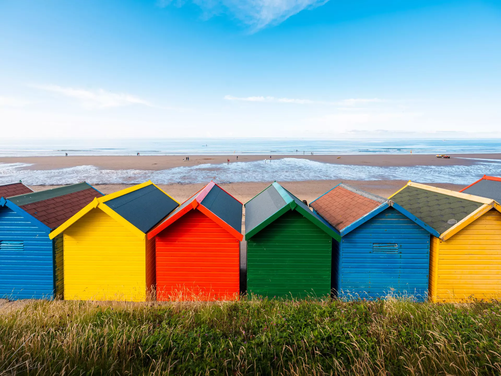 Brightly colored beach huts in reds, yellows, greens and blues facing a sandy beach.