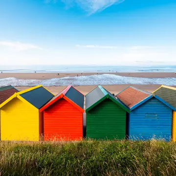 Brightly colored beach huts in reds, yellows, greens and blues facing a sandy beach.