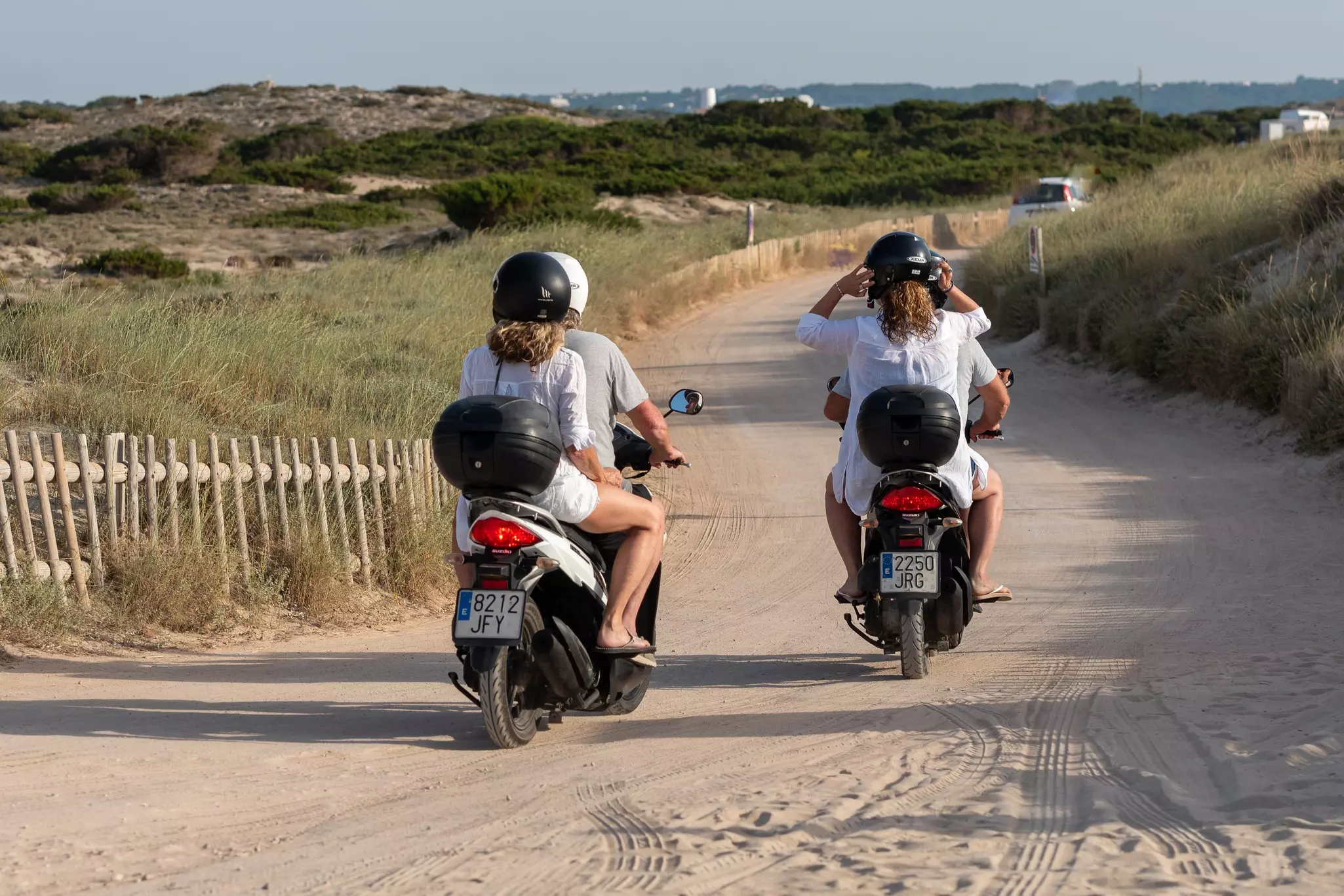 People riding motorbikes on a sandy track near a beach.