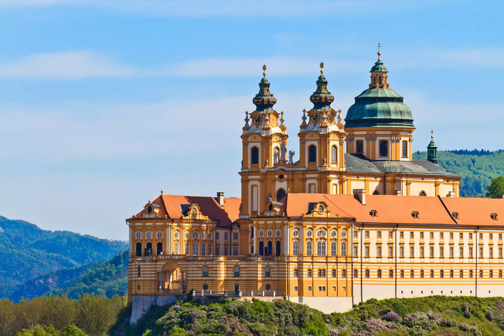 A large yellow building with white details, two spires and a dome.