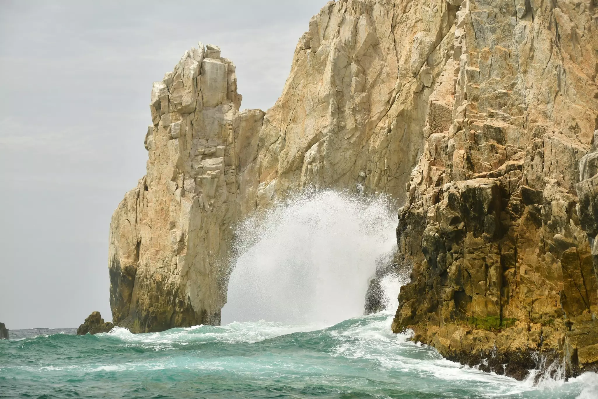 A huge wave throws up surf as it crashes against a craggy rock formation.