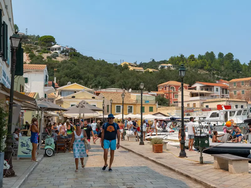 A bustling Greek port with yachts docked and people strolling by waterside restaurants