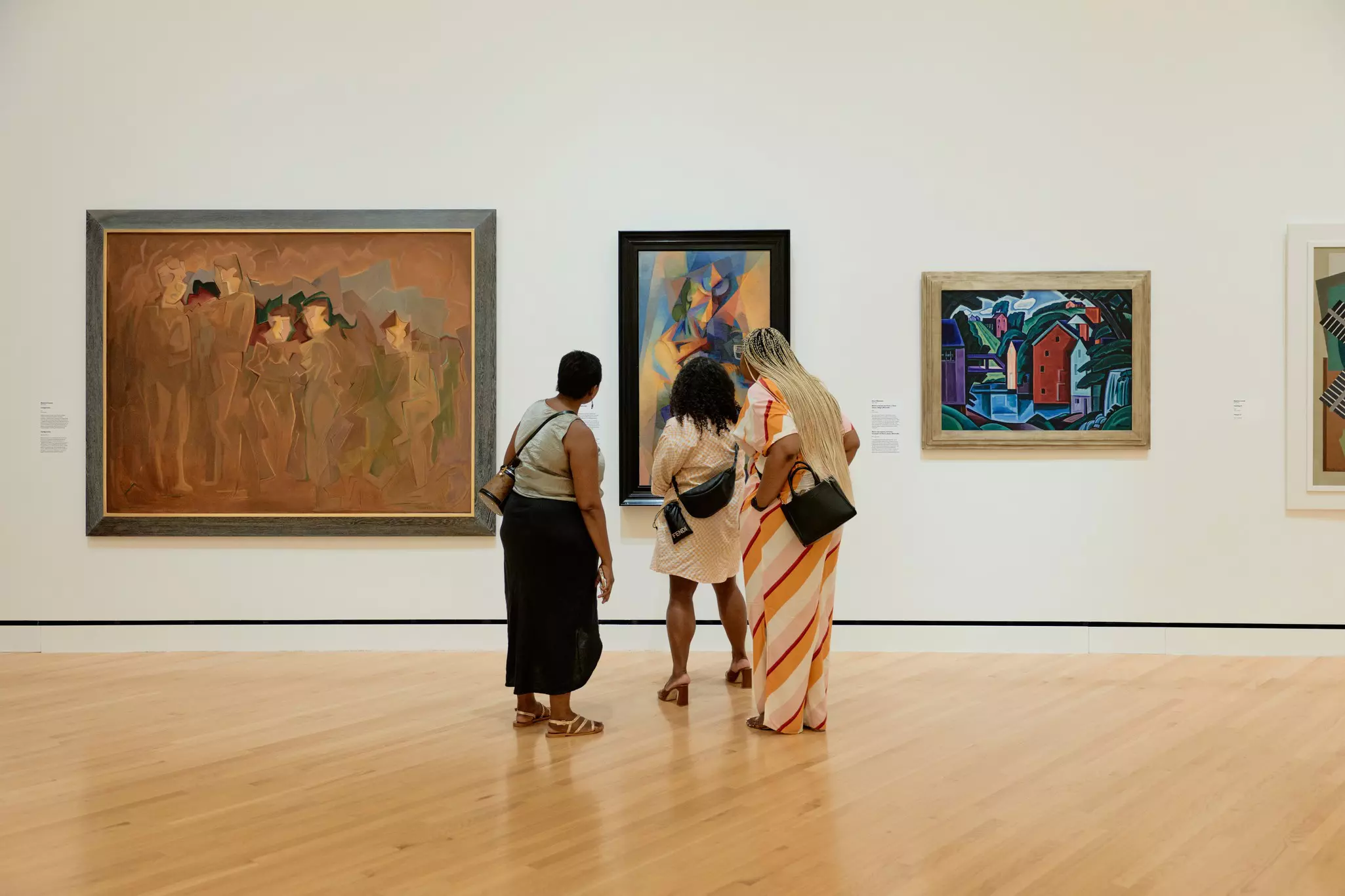 Three women look at art on a gallery wall.