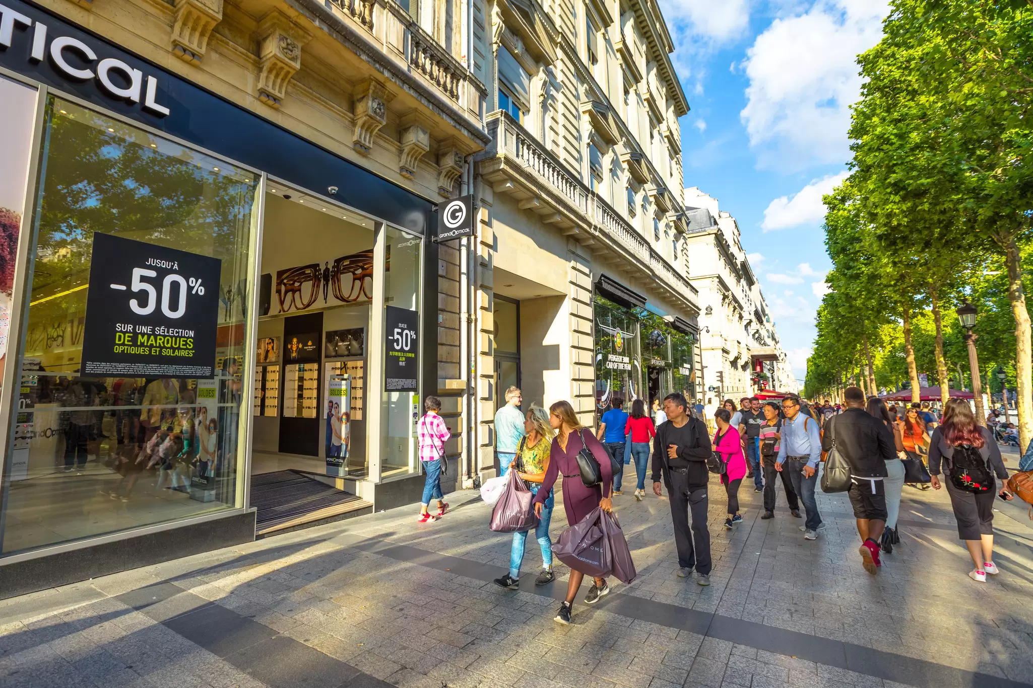 Tourists walk on the most famous avenue of Paris, the Champs Élysées, for shopping in luxury shops.
