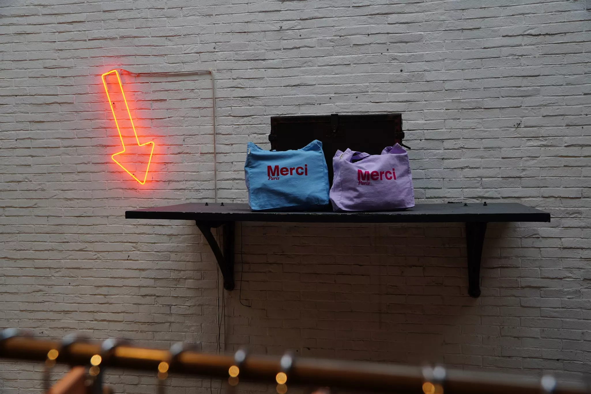 A red neon arrow points to two tote bags on a shelf at a retail store.