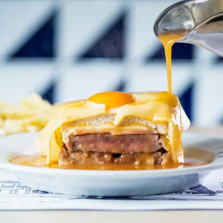 The francesinha, a sandwich with mortadella, two types of sausage, beef steak, ham, and cheese sandwiched in white bread, then topped with an egg, more cheese, and a spoonful of spicy tomato and beer sauce.