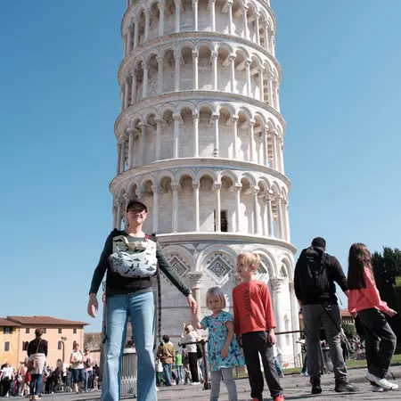 A woman and two small children stand in front of an ornate round tower that stands at an angle.