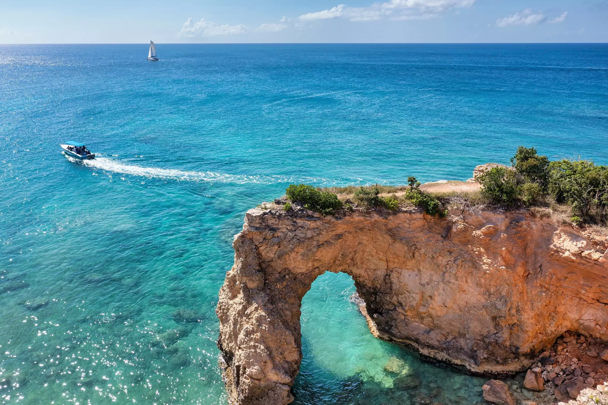 A tour boat sails near a natural rock arch formation
