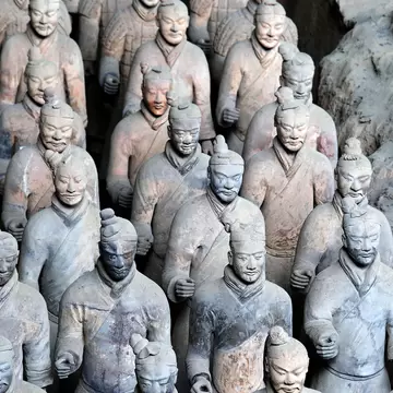 Rows of life-size terracotta infantry figures with topknots and robes standing in an earthen pit near Xi'an
