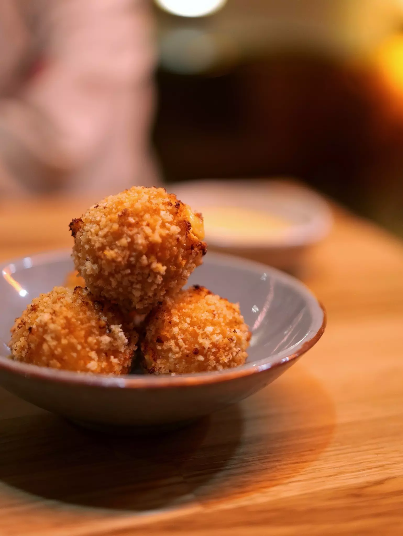 A small ceramic bowl with three deep-fried croquettes in it on a wooden table.