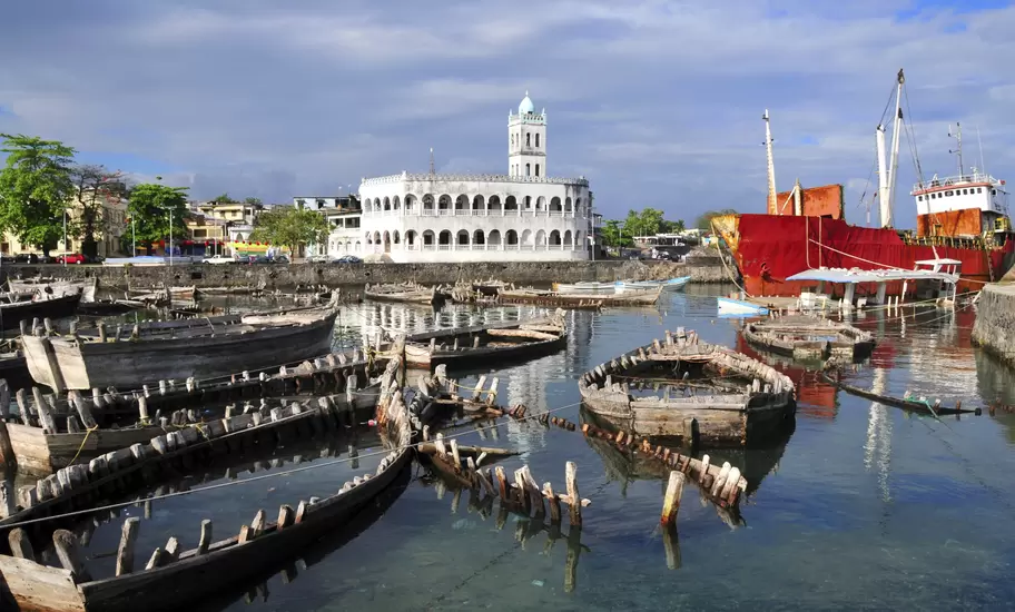 Whitewashed arcaded mosque with a minaret above Moroni harbour, Comoros, with wrecked wooden boats and a rusting red ship
