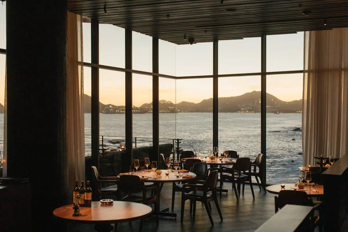 A restaurant with dining tables offers views of the ocean and mountains