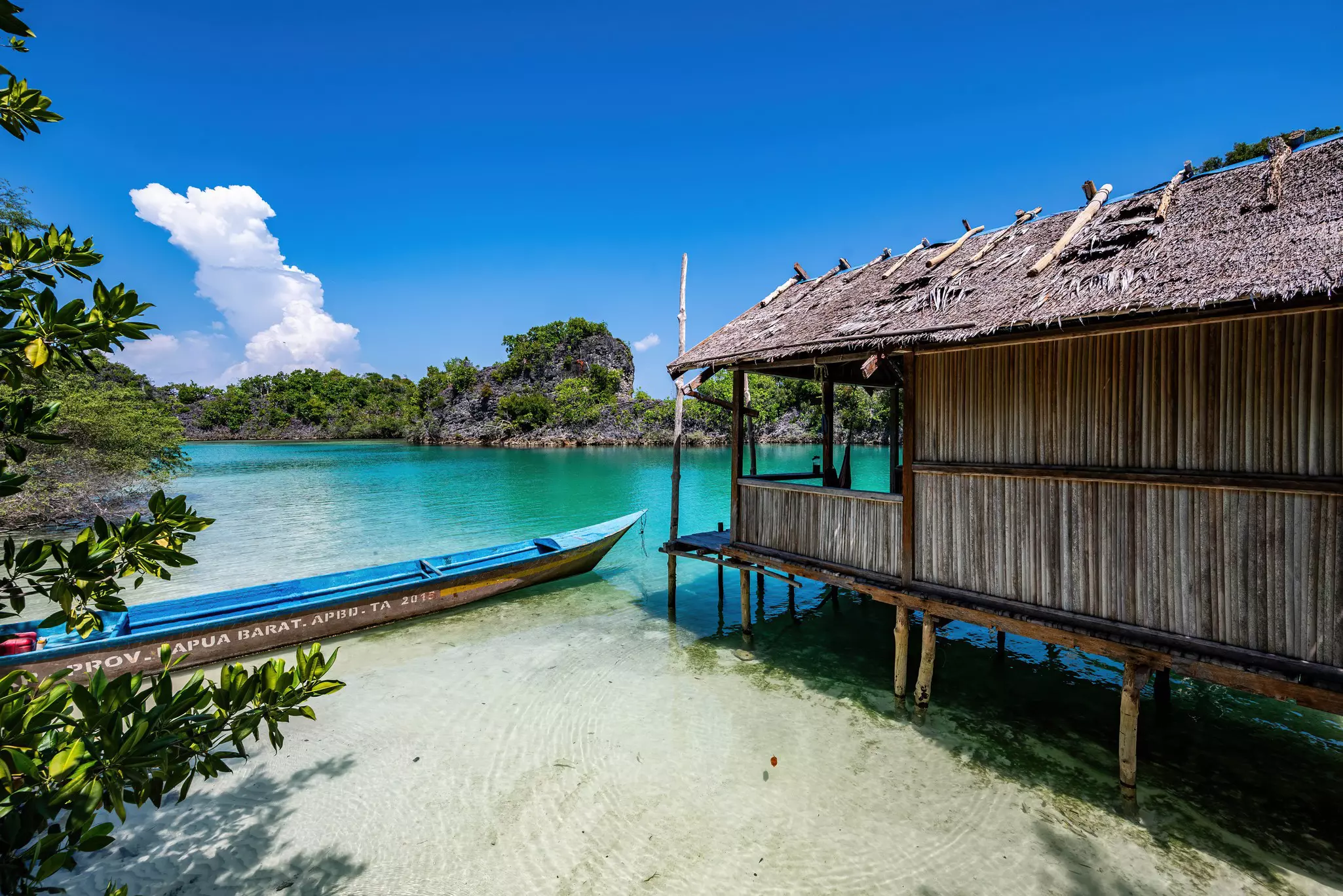 A boat sits next to an over water hut in an inland lagoon at Rufus Island in the remote Fam Islands of Raja Ampat