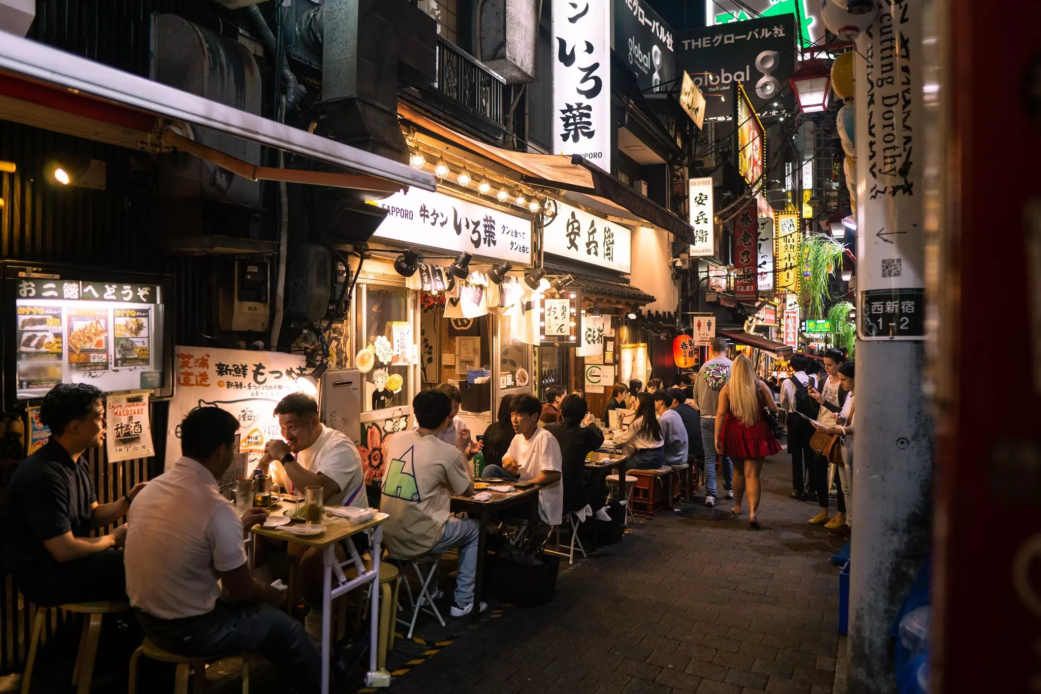 Tourists and locals enjoying drinks and skewers in a small alley of bars