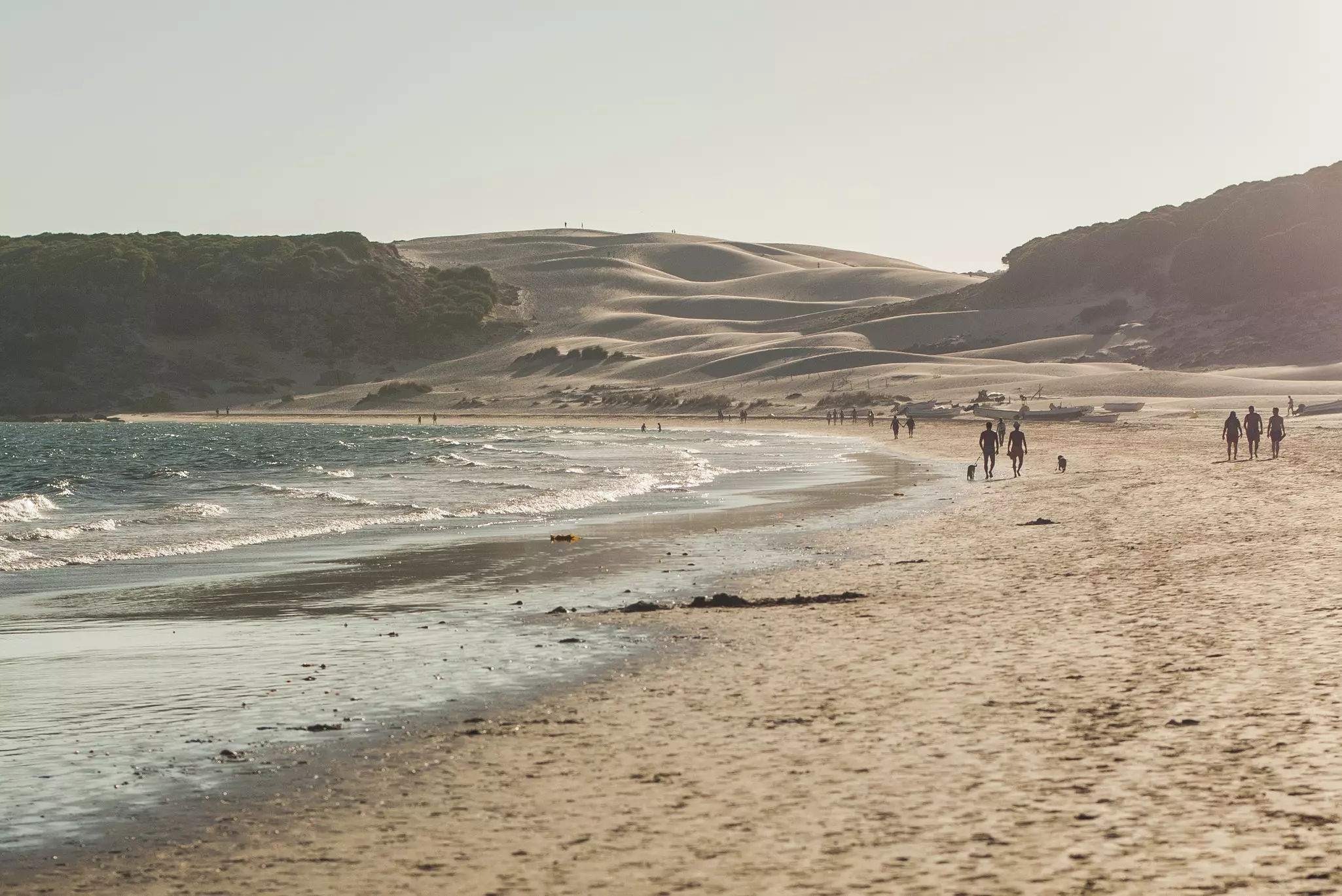 People walk along a golden sand beach backed by sand dunes