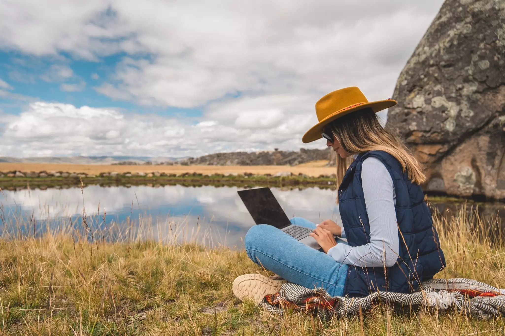A woman is sitting on the grass with a laptop in front of her in the Huayllay Stone Forest, Peru.