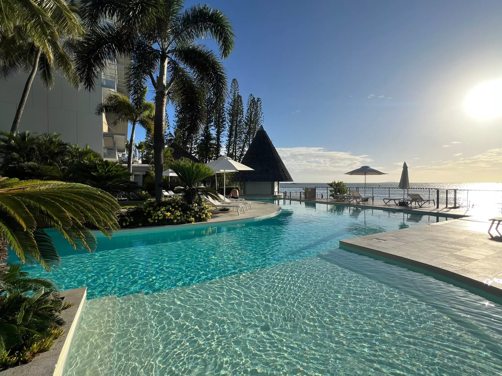 A hotel swimming pool and surrounding deck at the edge of the ocean.