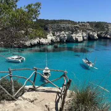 Sailboats anchored in the crystal clear turquoise waters of Cala Macarella on the island of Menorca, Spain.