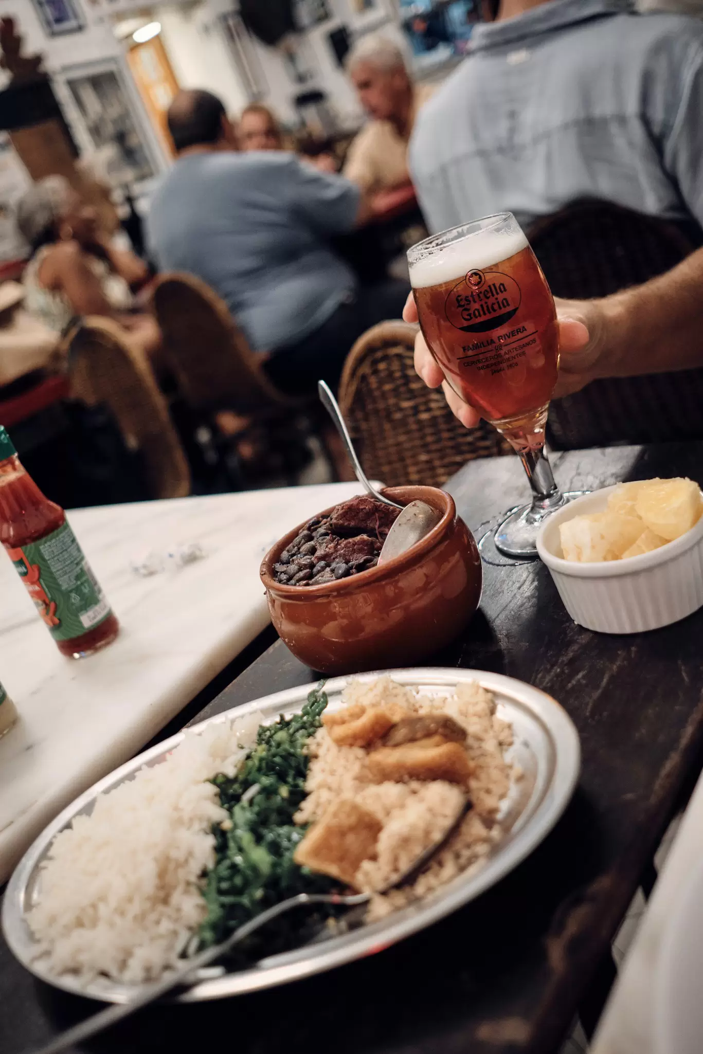 A round dish with black beans, a glass of beer and a plate of accompanying foods.