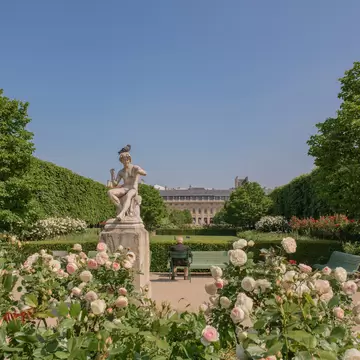 An older gentleman sits next to a statue in the garden at the Palais Royal building in Paris' Right Bank.
