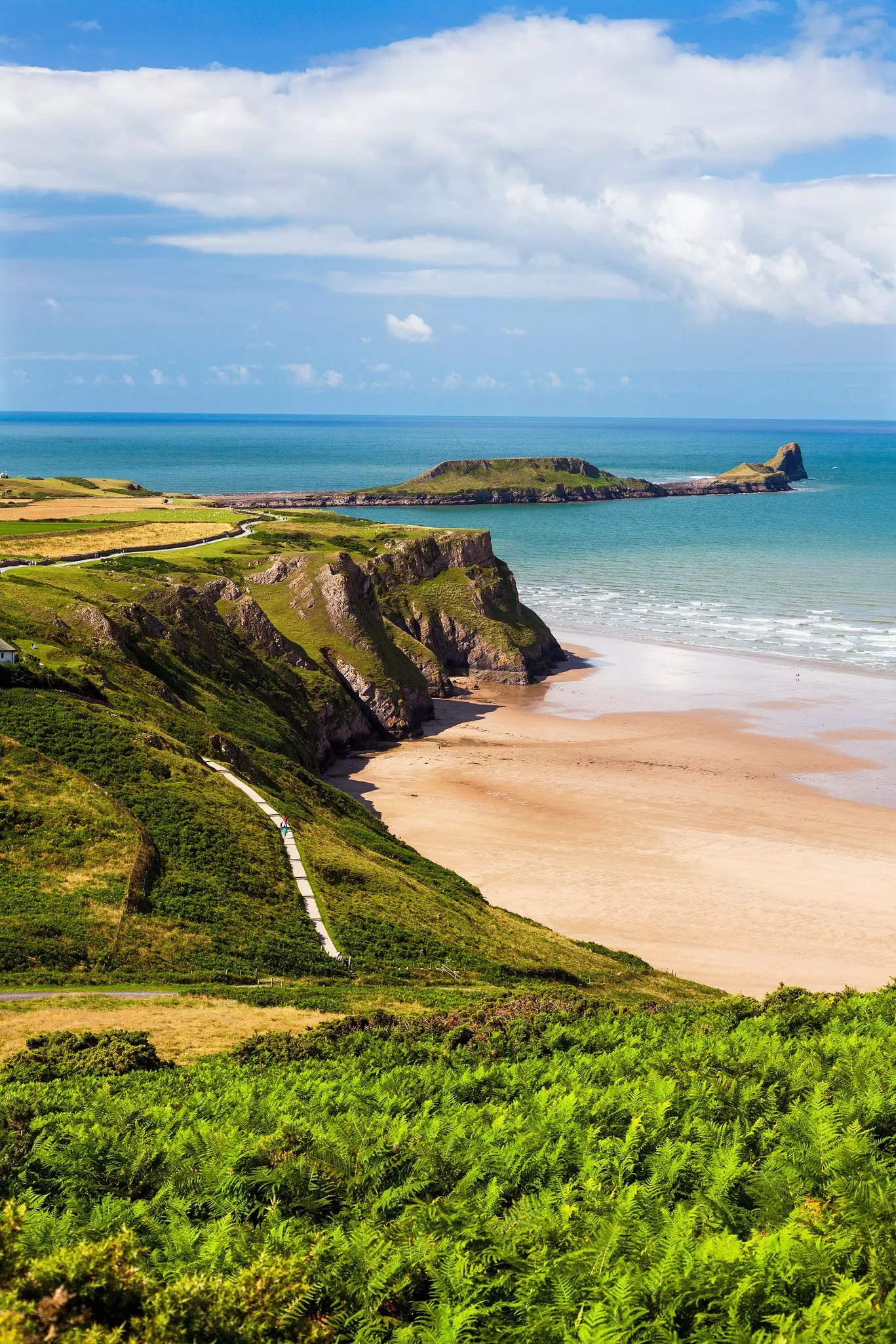 A sandy beach sheltered by cliffs with a rocky peninsula stretching out to sea.