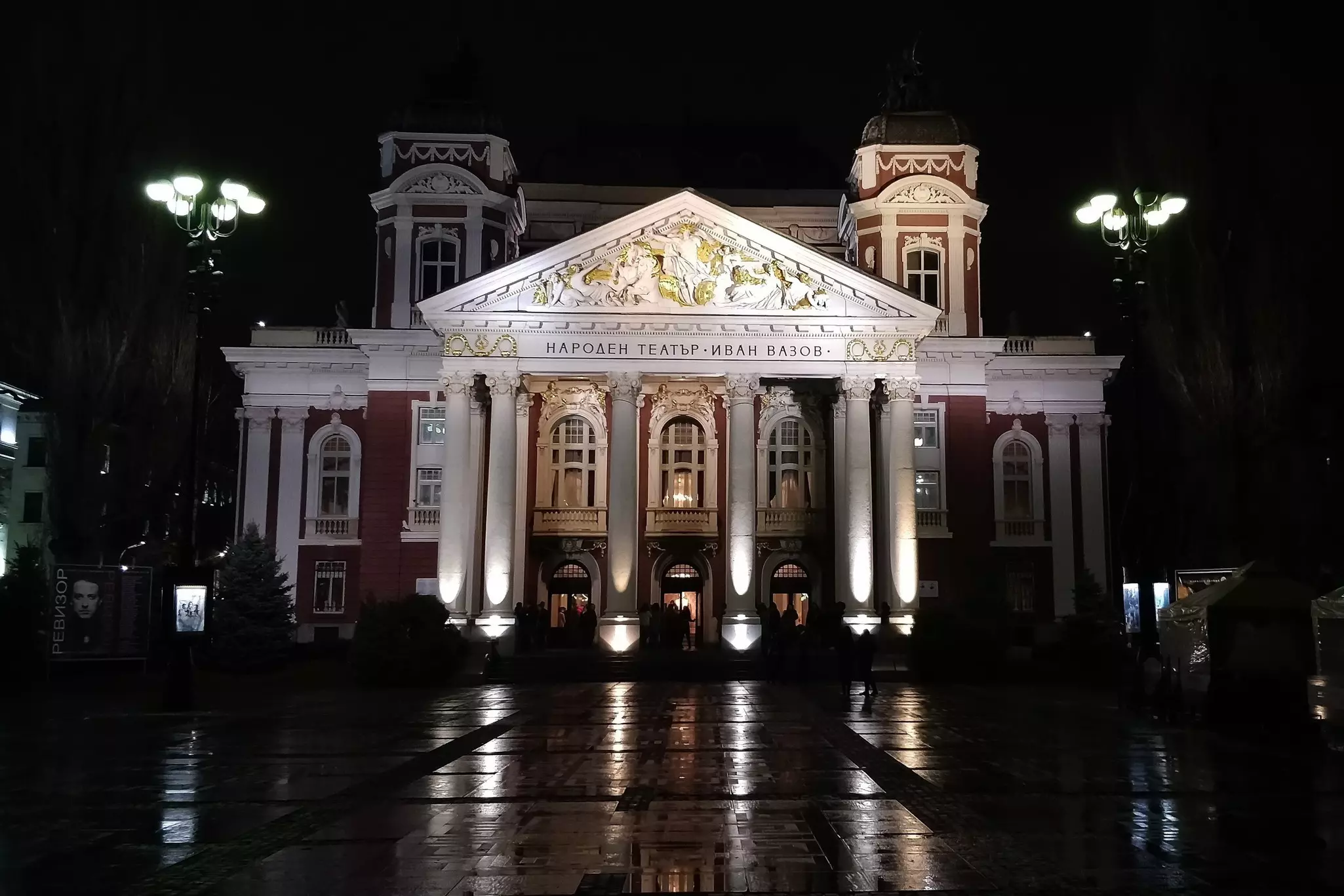 Exterior nighttime shot of a large red-coloured building, with a Greek-style columned exterior.