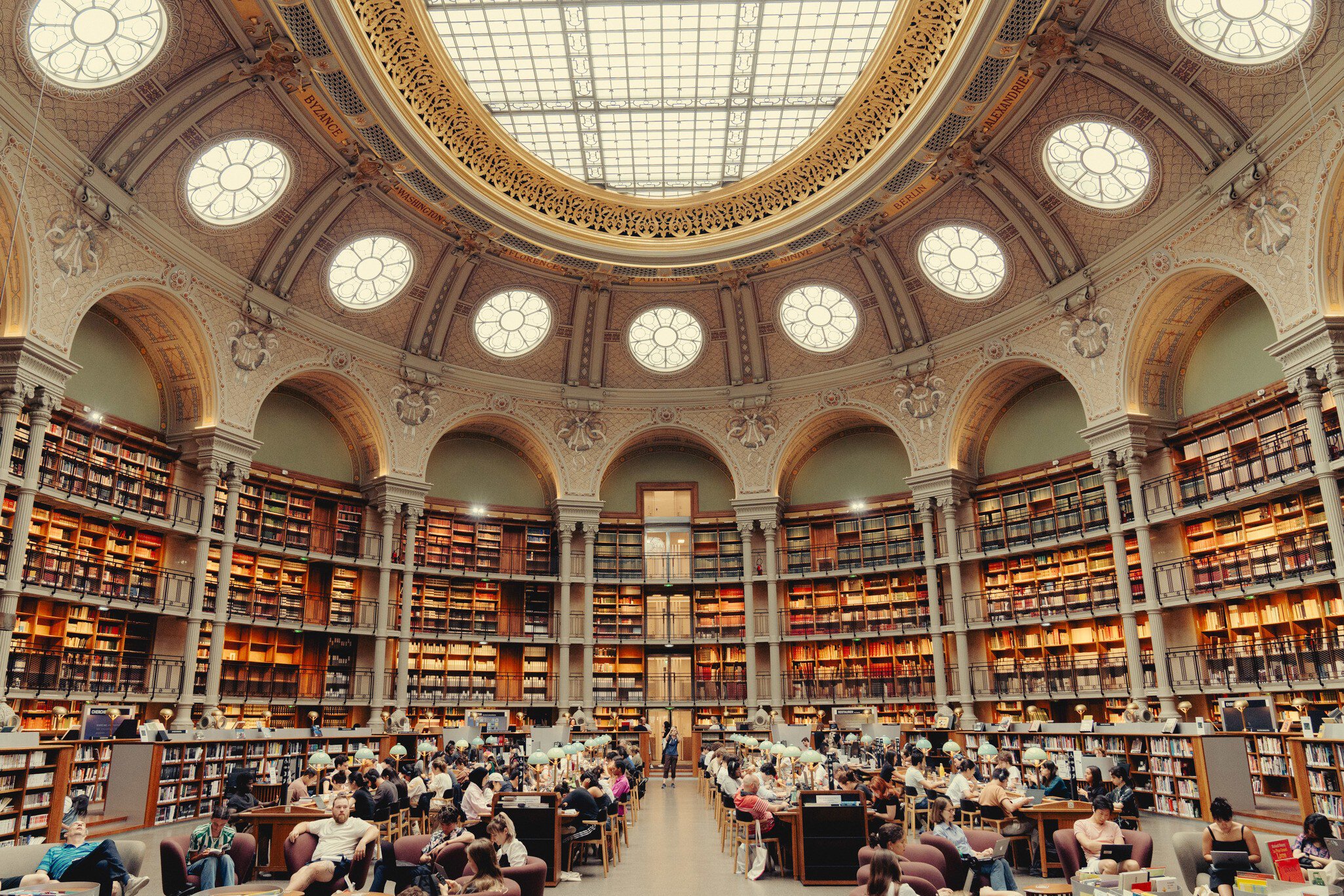 A vast library with desks and chairs under an ornate glass ceiling.